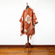 A poncho with geometric patterns drapes over a mannequin, displayed in a room with wooden flooring and a plain white wall.