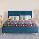A blue upholstered bed displays patterned bedding with geometric designs in red, blue, and white. It stands between two bedside tables with lamps in a softly lit, carpeted room.