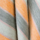 Tumbunuma baby alpaca wool blanket – a soft, woolen fabric drapes in folds, featuring diagonal stripes in shades of orange, gray, and cream, creating a cozy and warm appearance