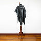 Nambija lightweight alpaca wool hooded poncho – a black and gray patterned poncho hangs on a wooden stand, displayed in a room with light hardwood floors against a plain white wall