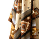 A patterned blanket hangs with geometric designs in brown, tan, and gray tones, featuring diamonds and zigzags. The background is plain, emphasizing the textile's intricate artwork.