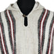 A woolen poncho with a hood, featuring vertical red, black, and white stripes, is displayed on a mannequin. It has a button closure at the neckline, against a plain background.