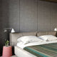 Jambue baby alpaca wool blanket – a neatly made bed with white pillows and a striped blanket stands against a textured gray wall. A side table with a small plant and a reading lamp provides ambiance