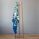 A patterned blue towel hangs on a minimalist wooden clothes rack in a room with light gray walls and a parquet floor.