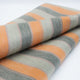 Tumbunuma baby alpaca wool blanket – a folded textile displays broad horizontal stripes in orange, gray, and cream. The fabric lies neatly on a plain, light surface, highlighting its soft texture and pattern