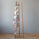 Sopoto baby alpaca wool blanket – a wooden blanket rack stands upright, holding a striped blanket and wire hanger, placed on a light wooden floor against a muted gray wall