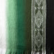 A woven fabric showcasing a gradient from white to dark green, with a geometric patterned stripe on the right, suggesting a traditional or decorative textile design.