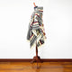 A mannequin is draped in a colorful, patterned poncho featuring geometric designs. It stands on a wooden floor against a plain white background.
