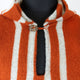 A woolen garment with orange and white stripes, featuring a wooden button at the collar, displayed on a black mannequin torso against a plain background.