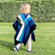 Wuachapa llama wool hooded poncho – a child wrapped in a striped poncho walks on green grass, with a background of dense greenery