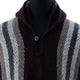 A knitted poncho with alternating brown, gray, and white vertical stripes covers a mannequin. It features a button at the collar, creating an opening. The background is white.