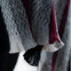 A close-up of a woolen fabric features vertical stripes in shades of gray, black, and red, displaying a textured and fuzzy surface, suggesting warmth and softness.