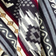 Geometric-patterned textile drapes, featuring zigzags, diamond shapes, and stripes in gray, black, white, and red tones, displayed with overlapping folds.