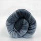 Gullian baby alpaca wool blanket – a rolled, multicolored grey wool blanket rests on a plain, white surface, displaying varying shades of grey in a spiral pattern