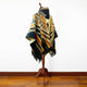 Shakai alpaca wool hooded poncho – a woven poncho with geometric patterns and earth tones drapes over a wooden mannequin stand, set against a plain white wall and hardwood floor