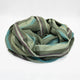 Jambue baby alpaca wool blanket – a striped blanket lies coiled on a plain white surface, featuring green, blue, and purple hues