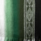 A woven textile displaying a gradient from white to green, featuring geometric patterns in a vertical stripe on the right, with a fringed edge at the bottom.