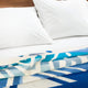 Two white pillows rest on a bed with a colorful, geometric-patterned blanket in blue tones, creating a modern and cozy bedroom setting.