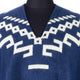 Blue knit sweater displayed on a mannequin, featuring geometric white patterns across the chest and shoulders, set against a plain background.