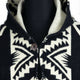 A black and white hooded sweater displays a geometric pattern with a visible button closure. It's shown on a black mannequin against a plain backdrop.