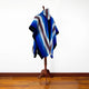 Wuachapa llama wool hooded poncho – a multicolored striped poncho drapes over a wooden stand, set against a plain white wall with a polished wooden floor
