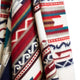 A colorful fabric features geometric patterns in red, blue, green, and brown tones, with repeating zigzags and lines, draped against a plain white background.