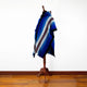 Wuachapa llama wool hooded poncho – a multicolored blue striped poncho drapes over a wooden stand, set against a plain white wall and hardwood floor