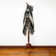 A black and white geometric-patterned poncho drapes over a wooden stand in a room with wooden flooring and a plain white wall.